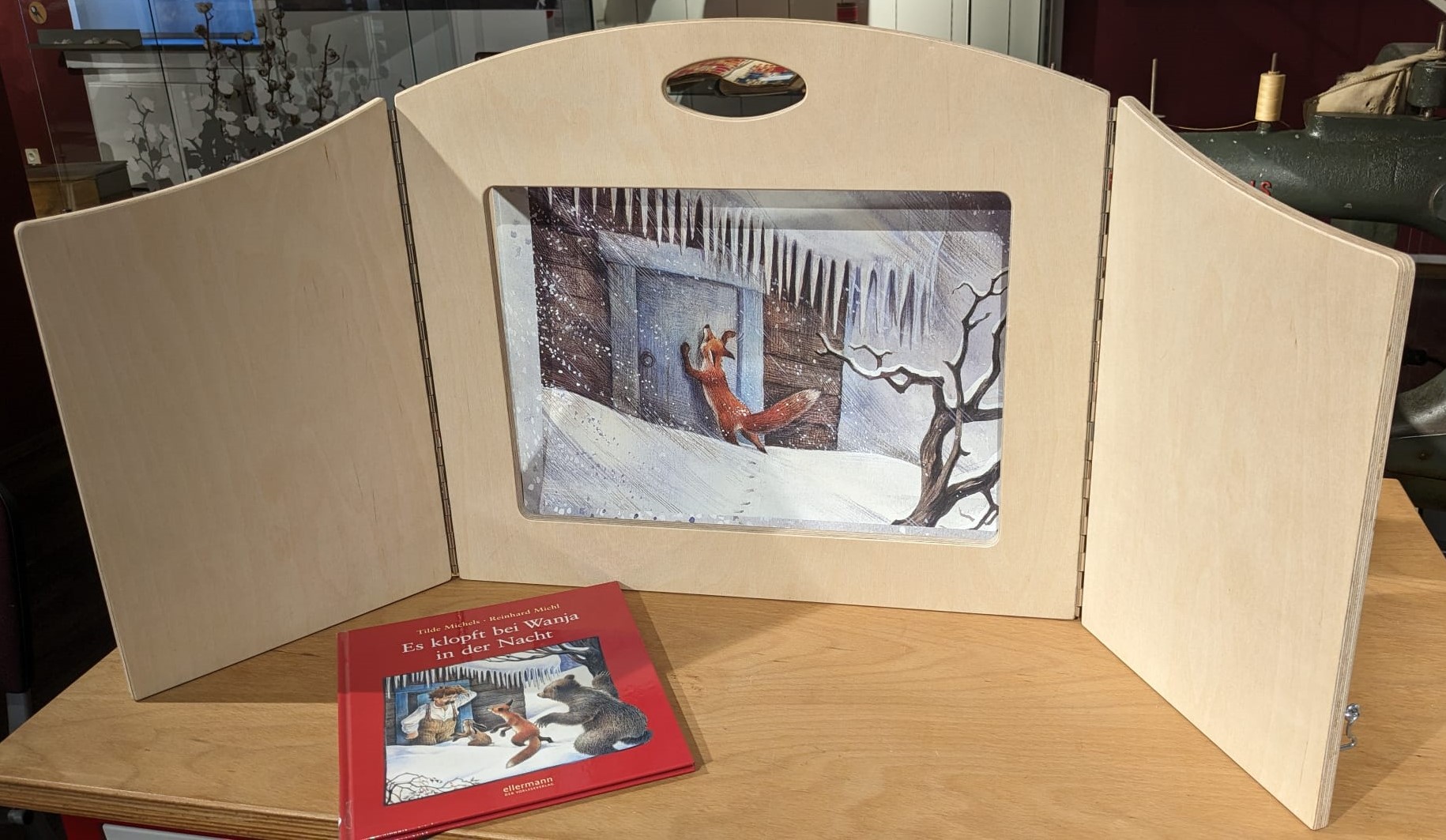 Bild in Holzrahmen. Davor liegt ein kleines Buch