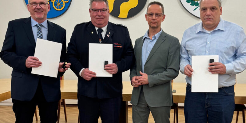 Vier Männer nebeneinander, drei mit Urkunden