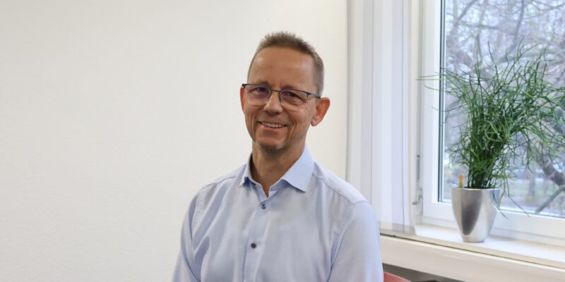 Mann sitzt in Büro und lächelt in die Kamera